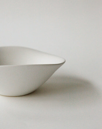 A minimalist white NR Ceramics HIN Soup Bowl with smooth curves sits on a plain surface, photographed against a light background. Only part of the bowl is visible, highlighting its simple, modern design by NR Ceramics.