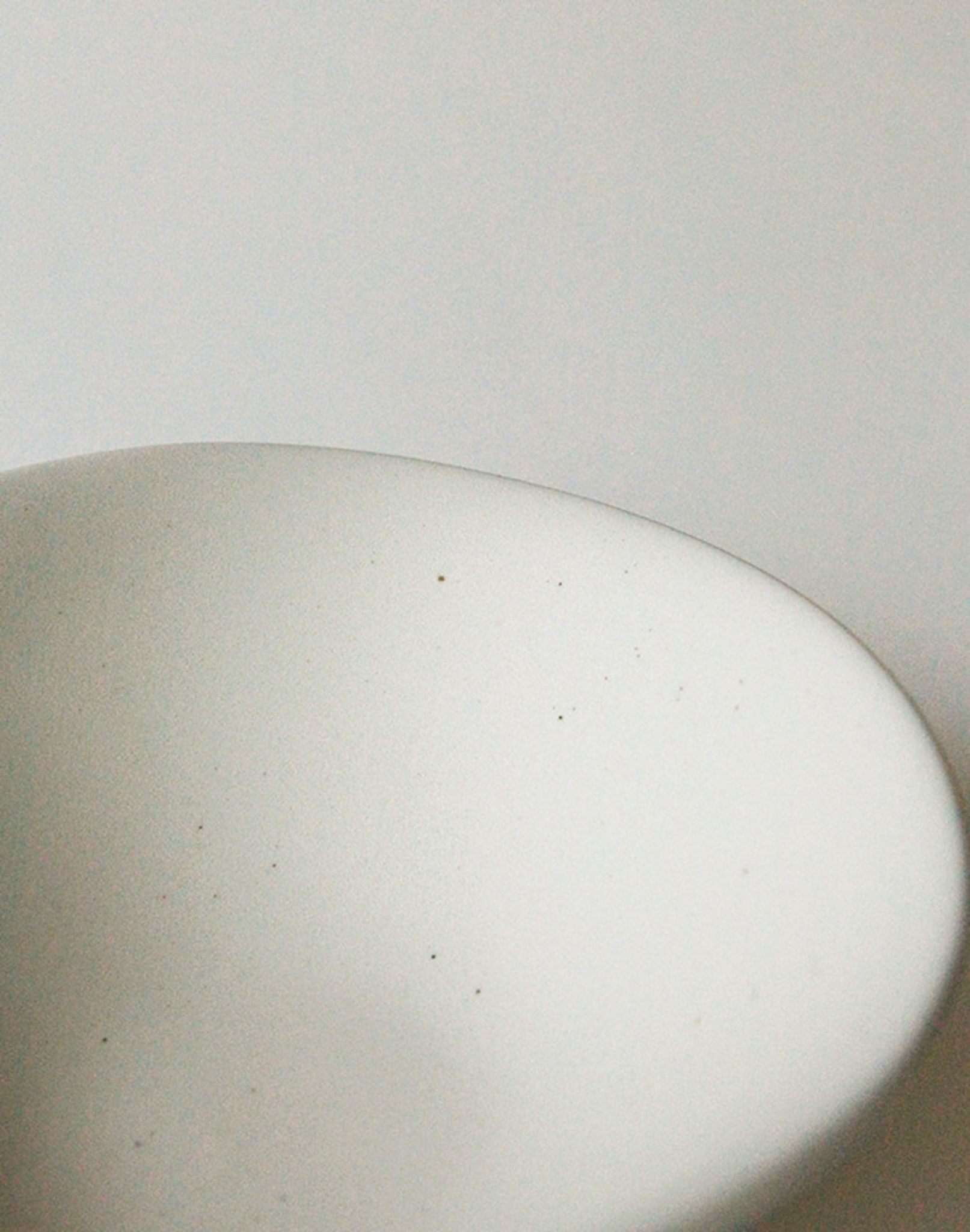 A close-up of the NR Ceramics HIN Soup Bowl by NR Ceramics—a smooth, white oval dish—set against a plain white background with soft lighting and tiny specks visible on its surface.