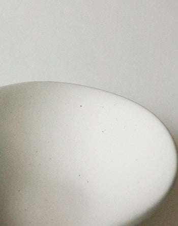A close-up of the NR Ceramics HIN Soup Bowl by NR Ceramics—a smooth, white oval dish—set against a plain white background with soft lighting and tiny specks visible on its surface.
