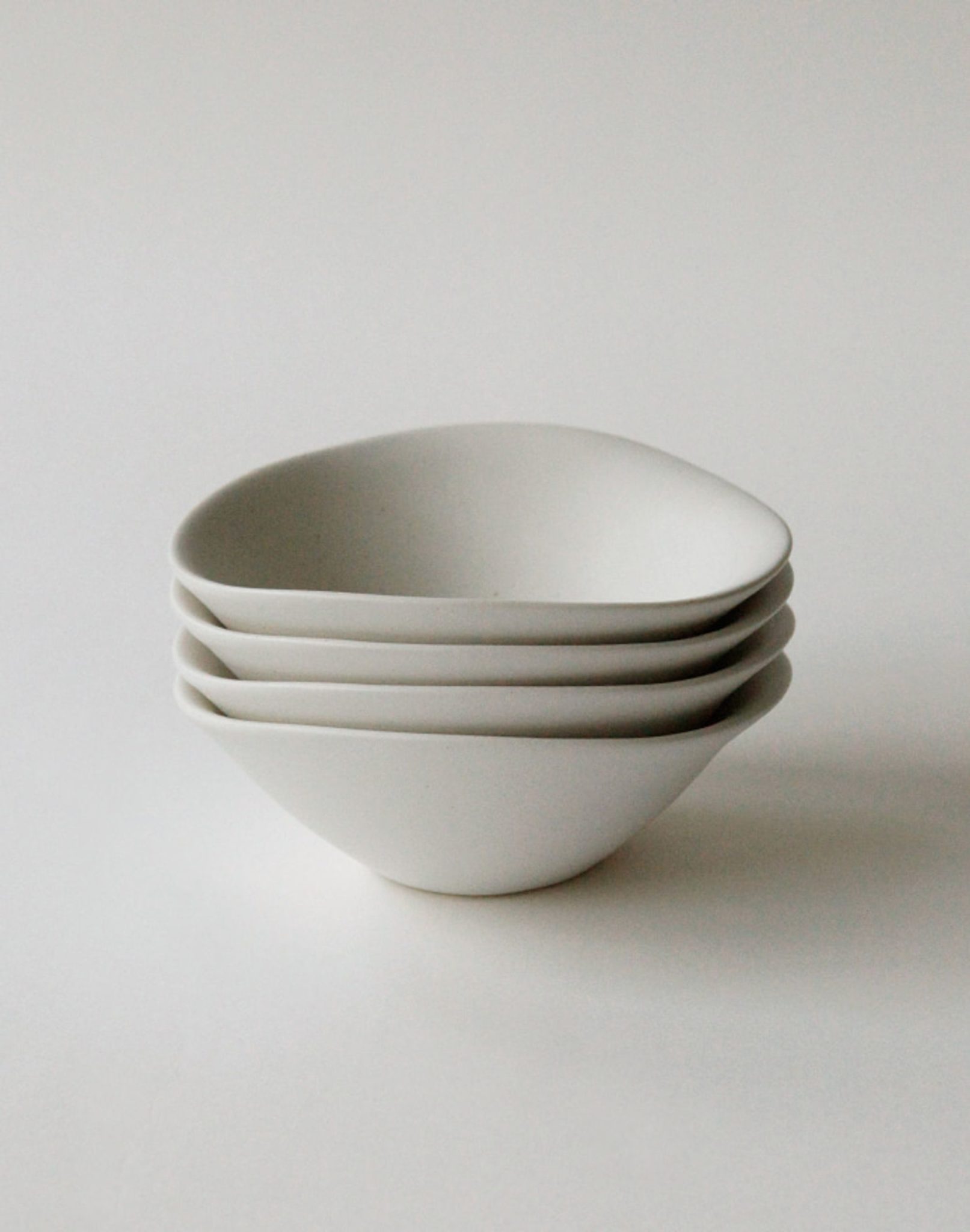 Four matte white NR Ceramics HIN Soup Bowls are stacked neatly on a white surface, showcasing versatile, modern tableware from NR Ceramics—ideal for soup or everyday use in a minimalistic setting.