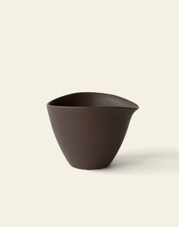 The NR Ceramics HIN Tea Cup by NR Ceramics is a dark brown ceramic piece featuring a minimalist, ergonomic design, small spout, and smooth matte finish, shown against a plain off-white background.