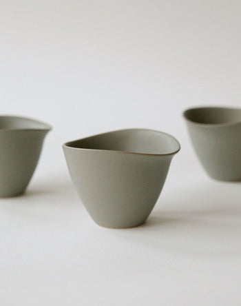 Three NR Ceramics HIN Tea Cups, featuring a minimalist matte grey finish and smooth, organic curves without handles, are elegantly arranged on a plain white background for a modern look.