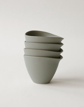 Four NR Ceramics HIN Tea Cups, featuring an ergonomic design with smooth curves and subtle spouts, are stacked neatly on a plain, light background.