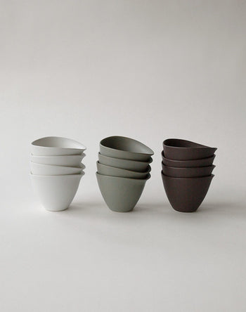 Three stacks of NR Ceramics HIN Tea Cups by NR Ceramics in white, gray, and dark brown—each with an ergonomic, minimalist design—are arranged four high on a plain light background.