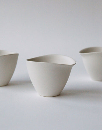 Three minimalist, white NR Ceramics HIN Tea Cups with irregular, organic shapes are arranged on a plain, light background. Their ergonomic design and thoughtful spacing create a clean, modern composition.