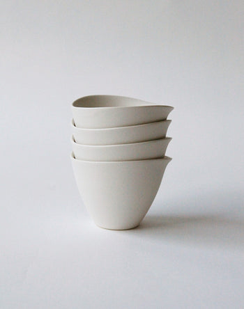 Four white NR Ceramics HIN Tea Cups are stacked neatly against a plain, light background. With a minimalist ergonomic design, smooth surfaces, and a slight spout, these cups by NR Ceramics blend style and functionality.