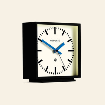 The Newgate Amp Mantel Clock is a modern square black mantel clock with a white face, black hour markers, blue hands showing 10:08, and classic station style. The NEWGATE brand name is printed on the clock face.