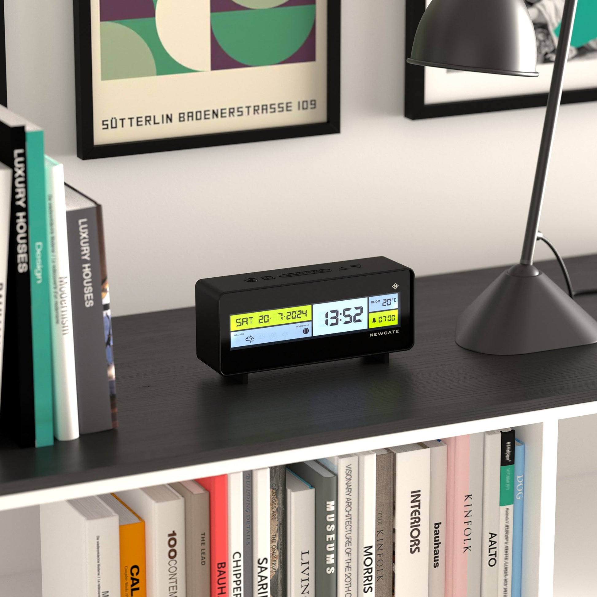 The Newgate Futurama LCD Alarm Clock by Newgate displays date, time, and temperature on a black bookshelf with books, a desk lamp, and framed art in a modern, organized room.