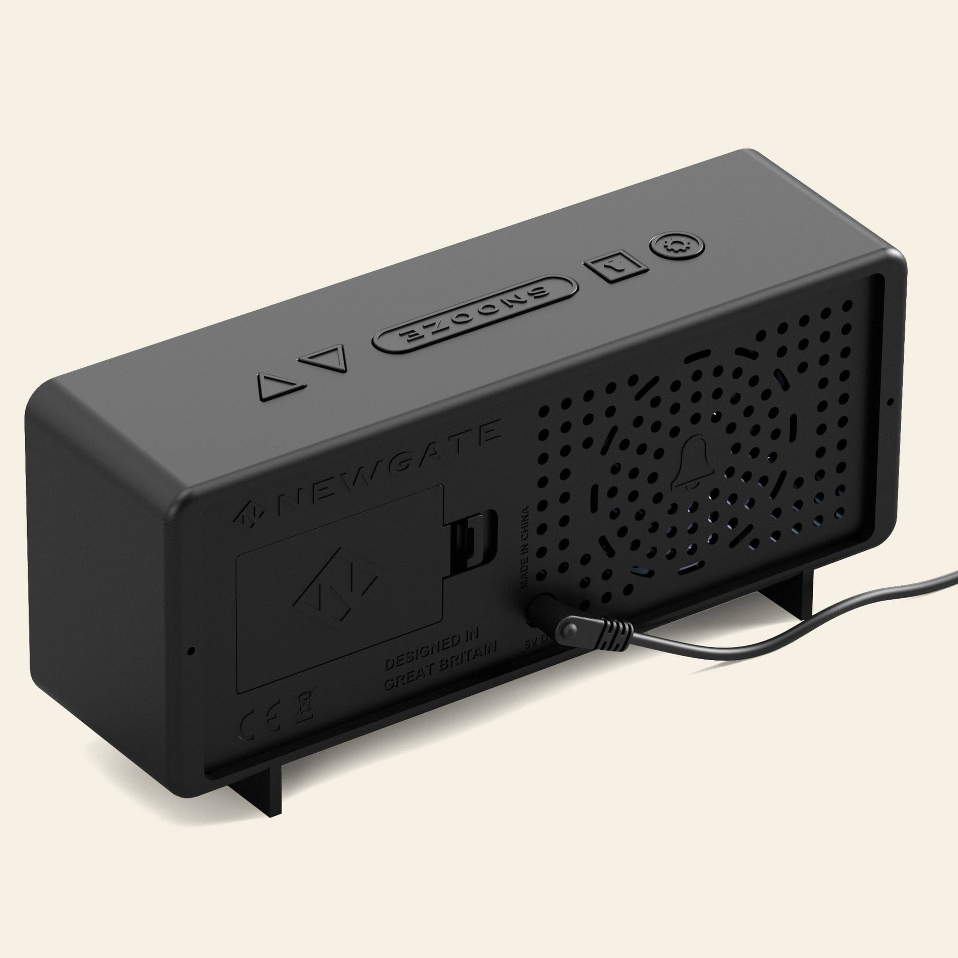The Newgate Futurama LCD Alarm Clock by Newgate is a black rectangular device with an LCD screen, perforated speaker grille, labeled buttons, a rear input port with a plugged-in cable, and design markings plus instructions on its surface.