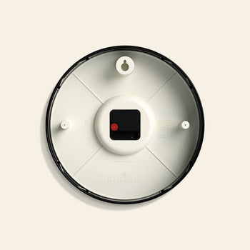 The image shows the back of the Newgate Luggage Wall Clock with a black frame, white interior, central battery compartment, two wall-mounting holes, and embossed Newgate branding near the bottom for a retro touch.