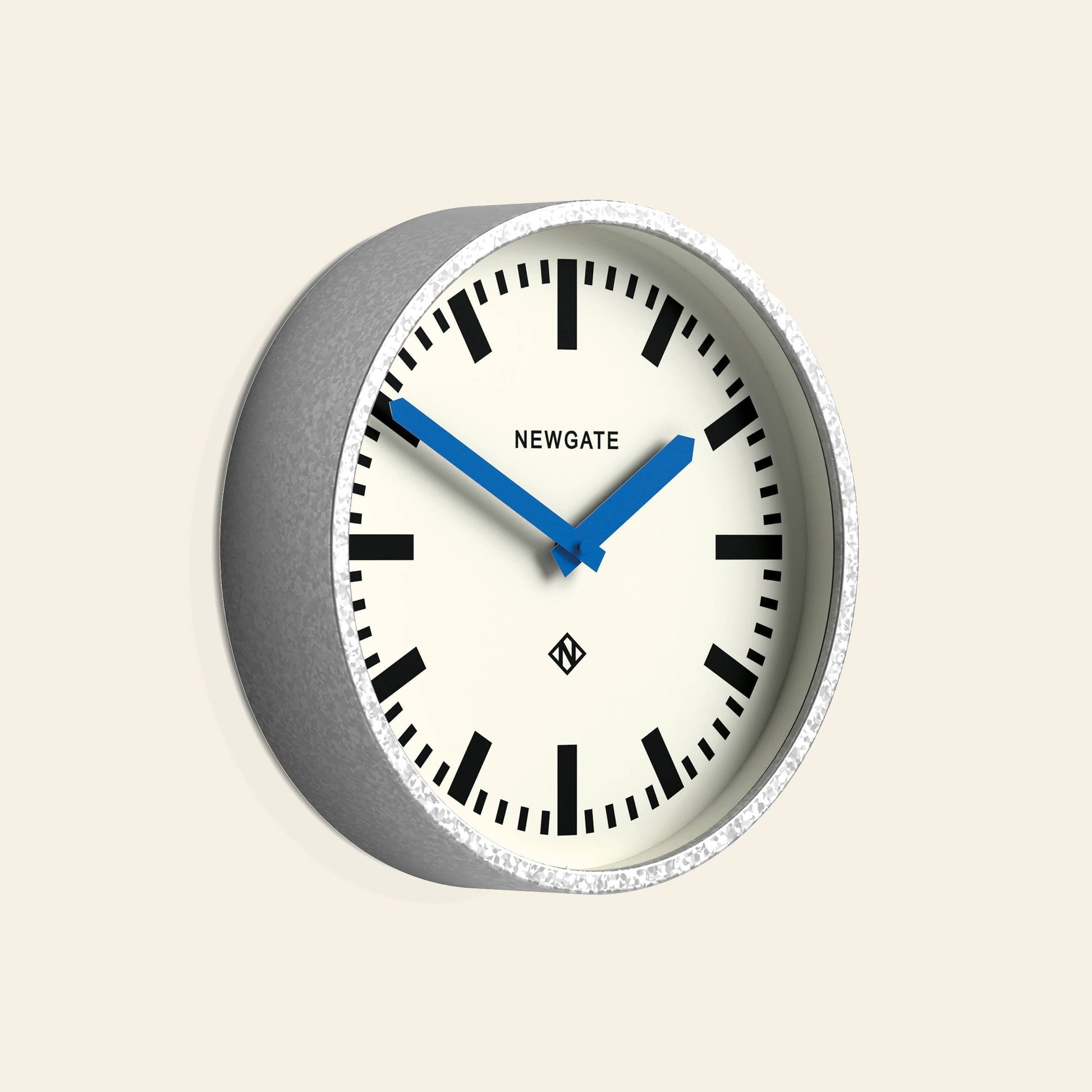 The Newgate Luggage Wall Clock Galvanised features a gray frame, white face, black markers, and blue hands. Inspired by mid-century railway station clocks, it displays the Newgate branding on its face.