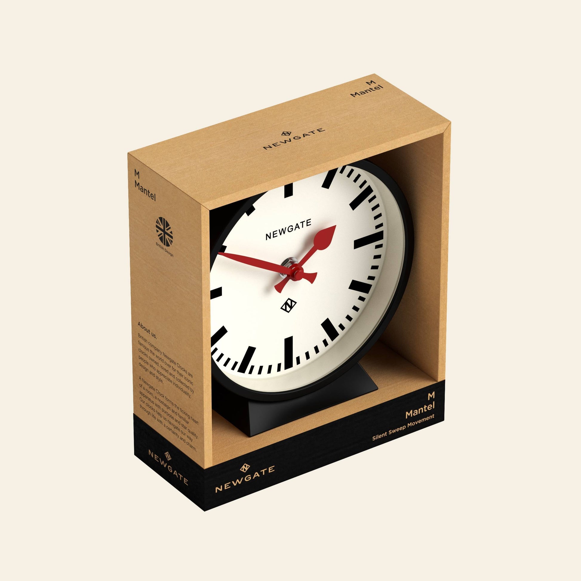 The Newgate M Mantel Railway Clock features a white face with black hour markers and red hands, packaged in minimalist brown and black cardboard bearing product details—a classic Newgate design.