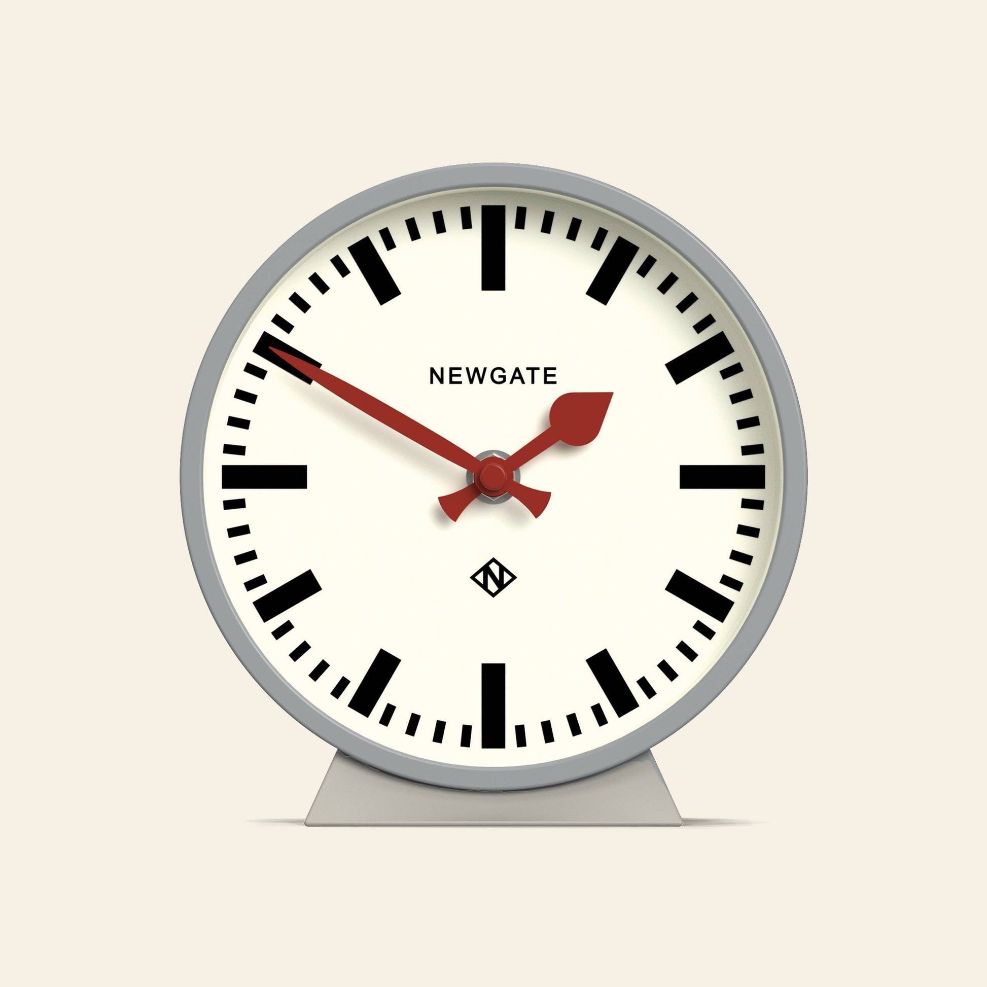 The Newgate M Mantel Railway Clock features a round analog design with a white face, bold black numerals, red hour and minute hands, a red second hand, and the NEWGATE brand name at the top center for a classic look.