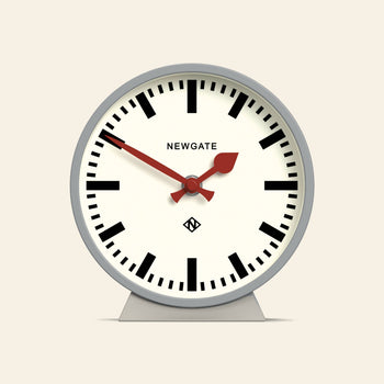The Newgate M Mantel Railway Clock features a round analog design with a white face, bold black numerals, red hour and minute hands, a red second hand, and the NEWGATE brand name at the top center for a classic look.