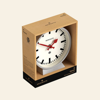 The Newgate M Mantel Railway Clock is a white station-style mantel clock with black hour marks and red hands, packaged in brown and black Newgate branding with a clear front to display its classic design.