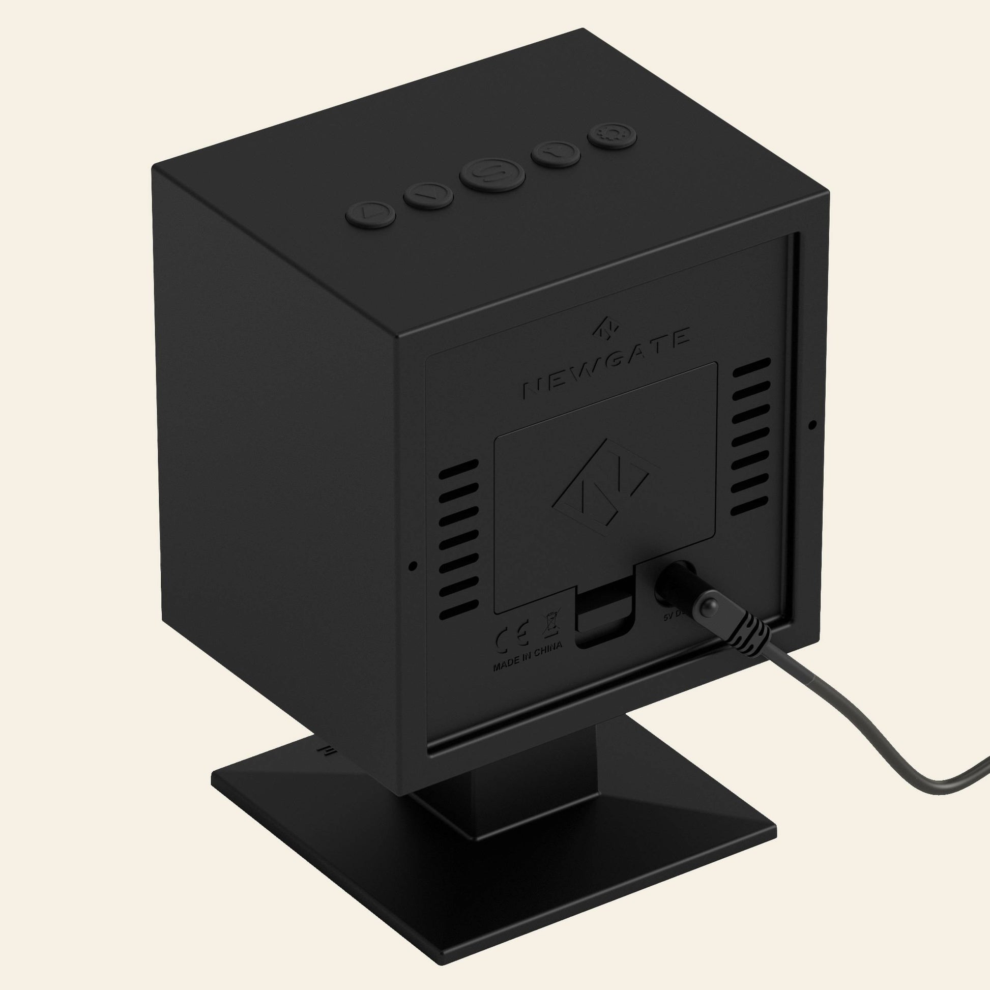 The Newgate Monolith LCD Alarm Clock by Newgate is a black, box-shaped clock with top buttons and a rear cord, shown on a square stand against a plain background.