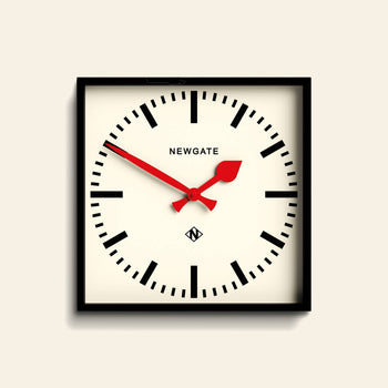 A minimalist black case frames the Newgate Number Five Railway Wall Clock, featuring a white face, bold black hour markers, vibrant red hands, and the Newgate logo at the top center. The time displayed is 10:08.