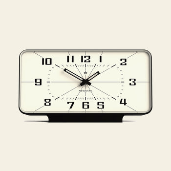 The Newgate Planet Mantel Clock features a rectangular black frame, bold Arabic numerals, and hands on a white face showing 10:10:31. The Newgate logo is below the center. It uses a silent sweep quartz movement for quiet operation.