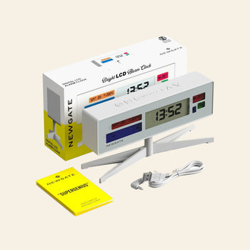 The Newgate Supergenius LCD Alarm Clock by Newgate, shown at 13:52, sits on its stand with a clear temperature display, alongside the packaging box, yellow instruction manual, and white USB power cable.