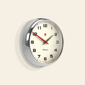 The Newgate Superstore Wall Clock features a round retro design with a cream face, black numbers, silver frame, black hour and minute hands, red second hand, and displays 10:08:37. Its vintage look is highlighted by the visible Newgate branding.