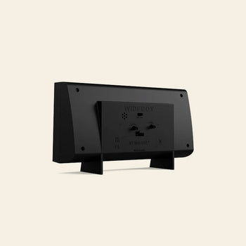 Rear view of the Newgate Wideboy Alarm Clock by Newgate, a black rectangular retro-style alarm clock with two support legs and detailed ports, labels, and text on its back, displayed on a plain beige background.