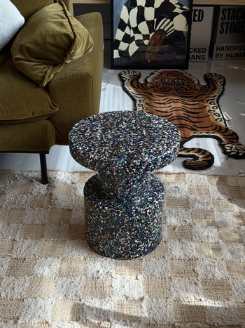 Close-up of the Normann Copenhagen Bit Stool, featuring a terrazzo-inspired surface with small, colorful specks on dark material. This multifunctional piece by Normann Copenhagen has smooth, rounded edges and a matte finish.