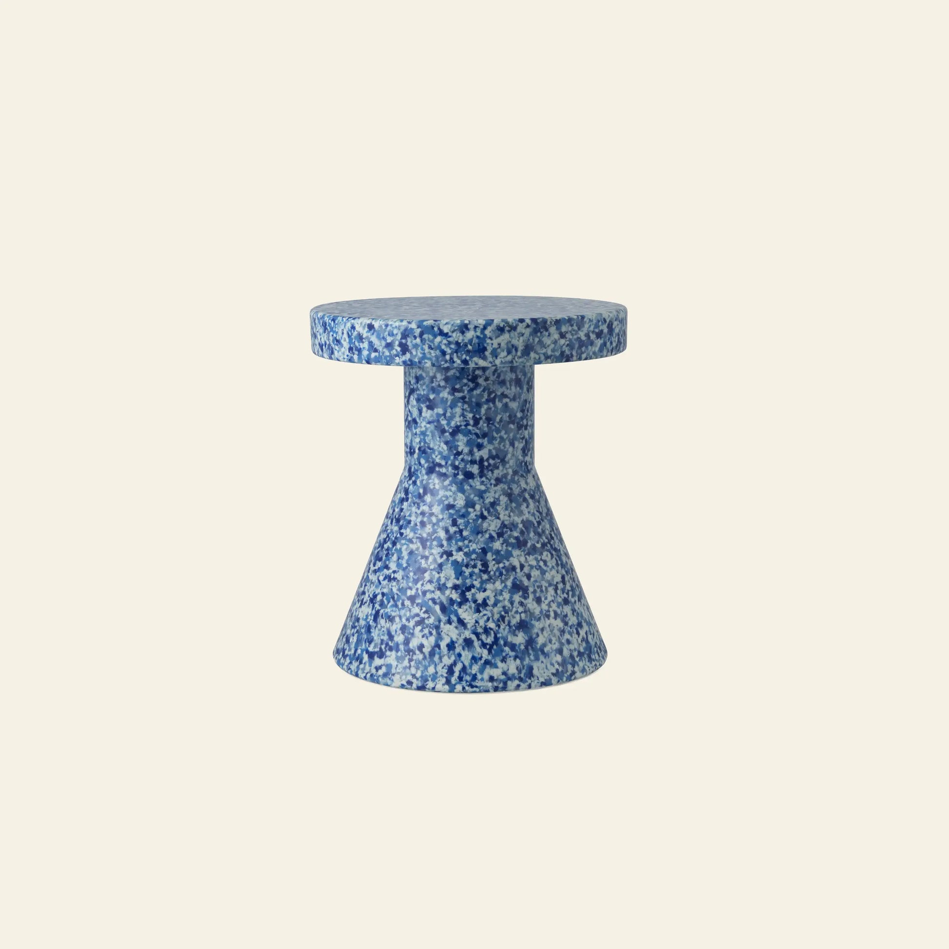 The Normann Copenhagen Bit Stool Cone features a small, round silhouette with a flared base, speckled in blue and white hues. Its multifunctional design works as a side table or extra seating, shown against a plain cream background.