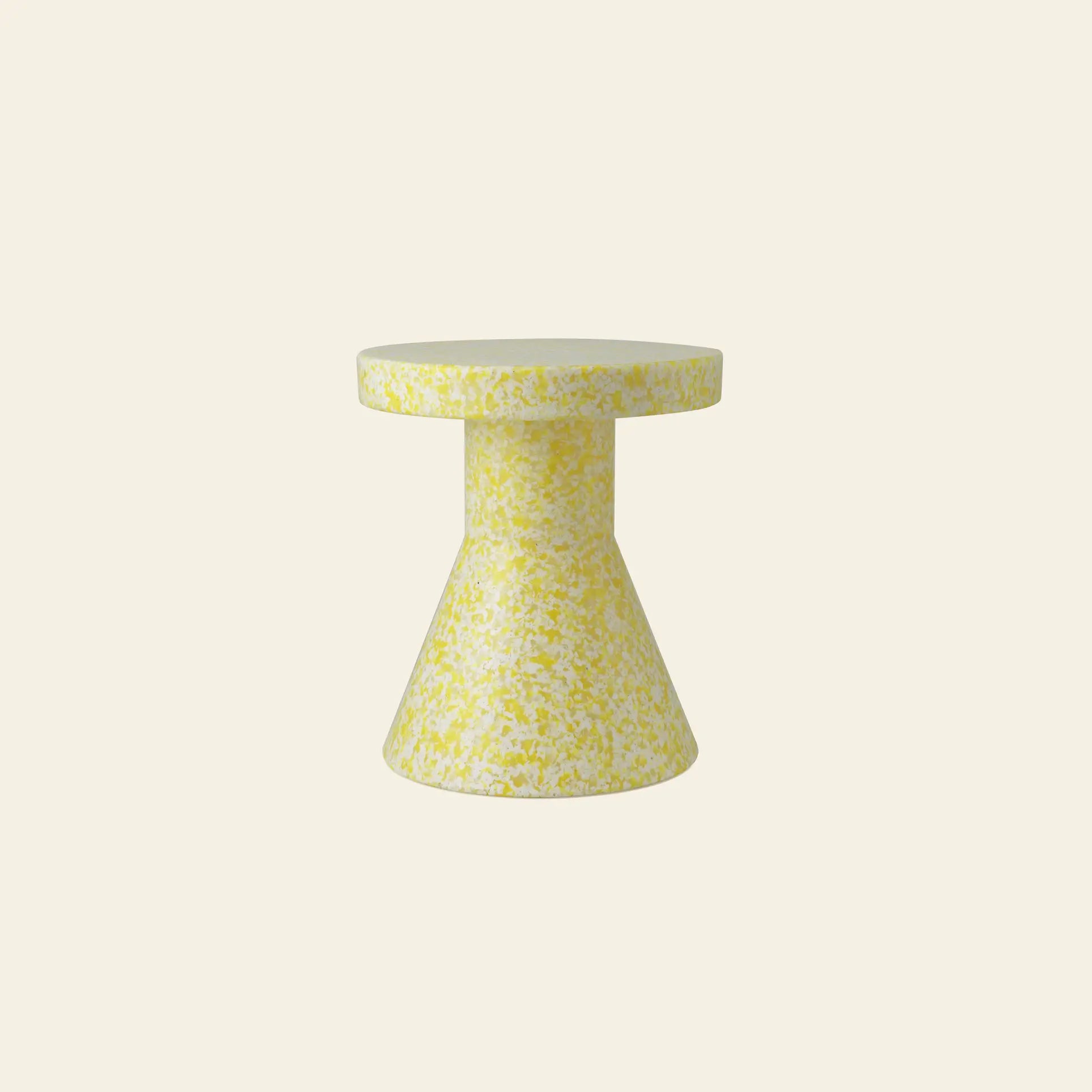 The Normann Copenhagen Bit Stool Cone by Normann Copenhagen features a small, round shape with yellow and white speckles. Its cylindrical top and cone-shaped base allow it to function as both a side table and versatile seating on a plain light background.