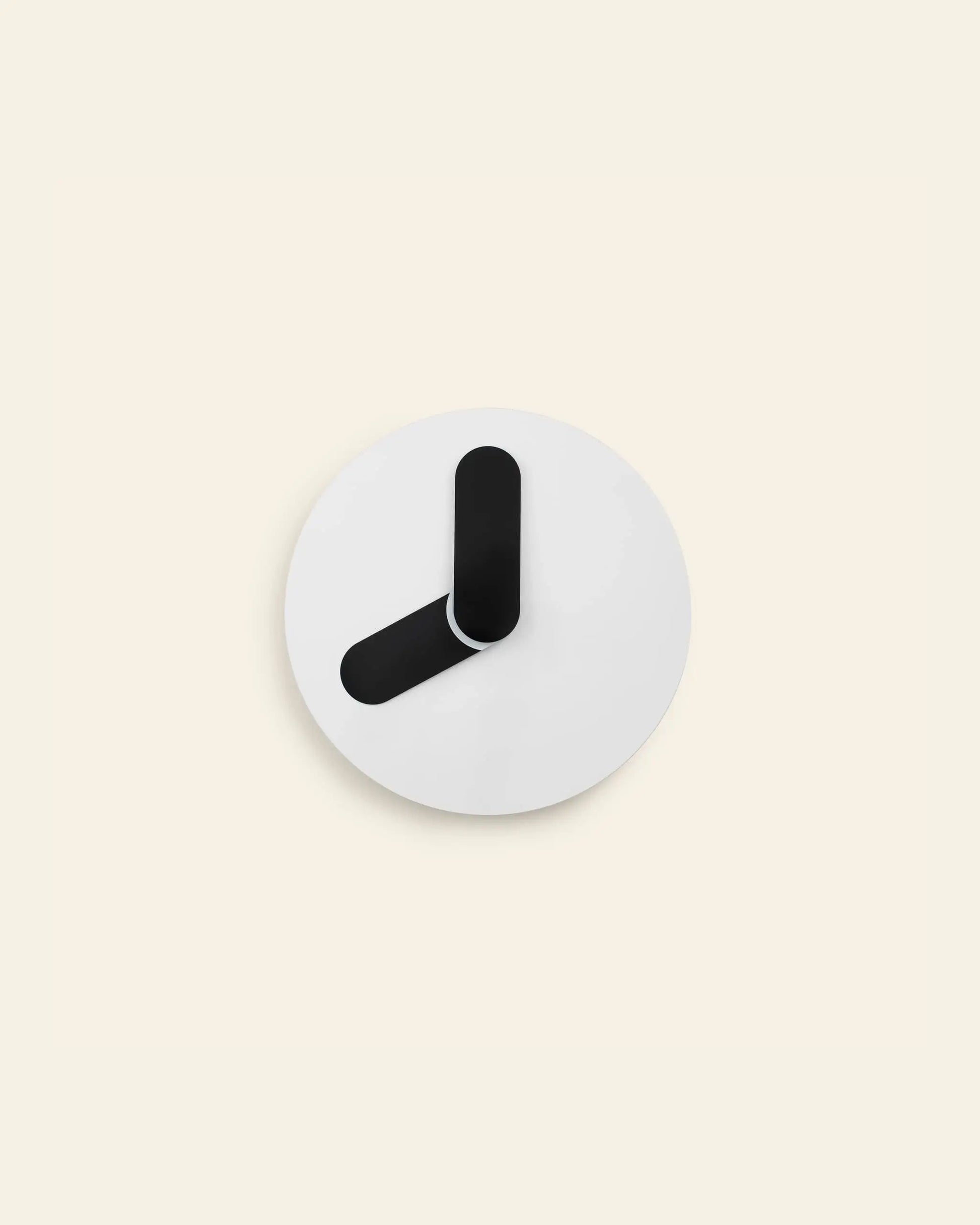 The Normann Copenhagen Bold Wall Clock by Normann Copenhagen showcases a minimalist round design with a white face and two thick, black hands. The clock has no numbers or markings, embracing pure minimalism against a light beige background.