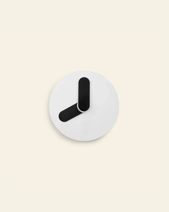 The Normann Copenhagen Bold Wall Clock by Normann Copenhagen showcases a minimalist round design with a white face and two thick, black hands. The clock has no numbers or markings, embracing pure minimalism against a light beige background.