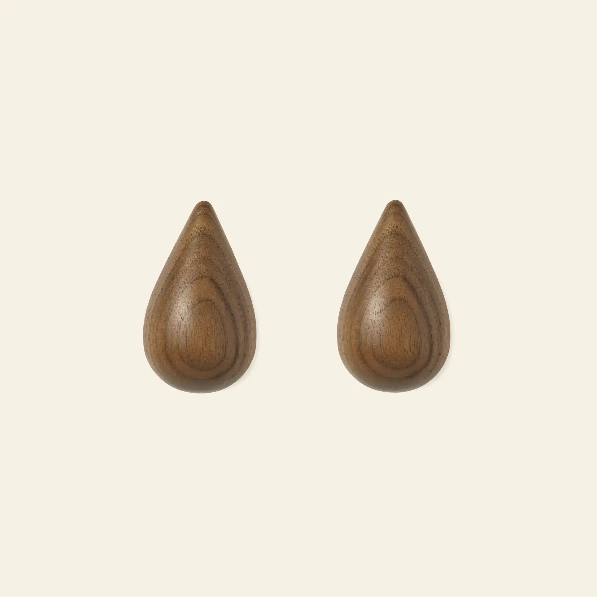 Two Normann Copenhagen Dropit Hooks Small, Set of 2, are mounted side by side on a light background. With a drop-shaped design and smooth wooden finish, theyre available in oak or dark walnut to bring a stylish touch to any space.