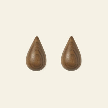 Two Normann Copenhagen Dropit Hooks Small, Set of 2, are mounted side by side on a light background. With a drop-shaped design and smooth wooden finish, theyre available in oak or dark walnut to bring a stylish touch to any space.