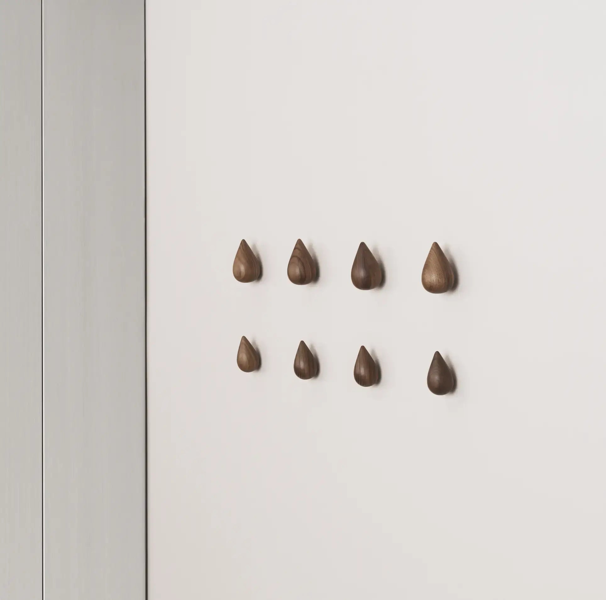 A set of two large, teardrop-shaped Normann Copenhagen Dropit Hooks adds bold, wooden elegance to a white wall, creating a stylish accent from the renowned Normann Copenhagen brand.