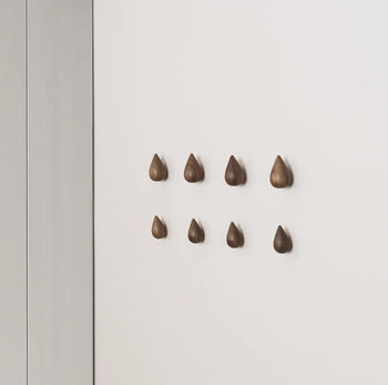 A set of two large, teardrop-shaped Normann Copenhagen Dropit Hooks adds bold, wooden elegance to a white wall, creating a stylish accent from the renowned Normann Copenhagen brand.