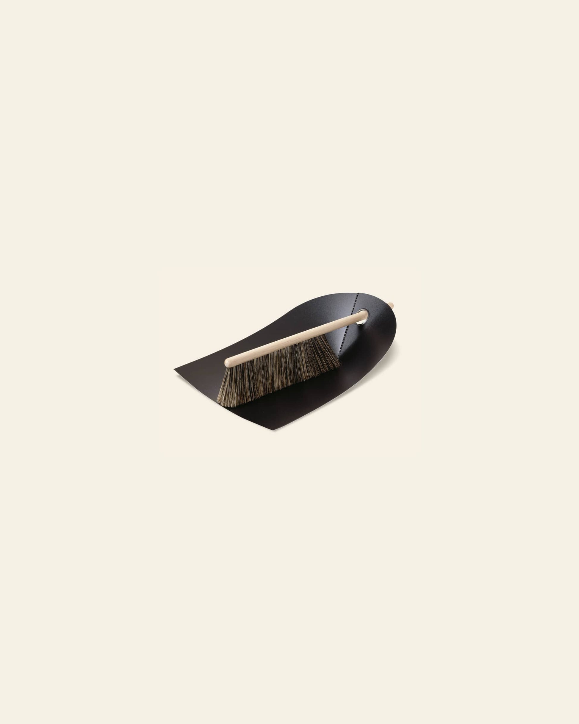 The Normann Copenhagen Dustpan & Broom set, featuring a black dustpan and wooden-handled brush with dark bristles, is arranged on a light beige background to highlight its compact size and practical design.