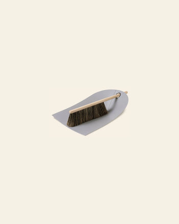 The Normann Copenhagen Dustpan & Broom features an ergonomic design with a wooden-handled brush and dark bristles resting neatly on the compact dustpan by Normann Copenhagen.