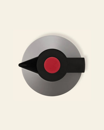 A top-down view of the Normann Copenhagen Geo Vacuum Jug, a modern round gray teapot with a black spout and handle, a large red knob on the lid, and a vacuum-insulated body, set against an off-white background.