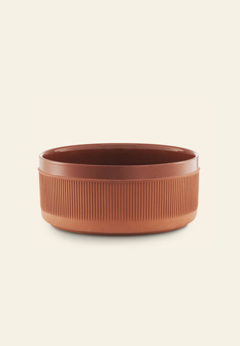The Normann Copenhagen Junto Bowl, 24cm, features a round, rustic terracotta design with vertical grooves on the exterior, shown against an off-white background.