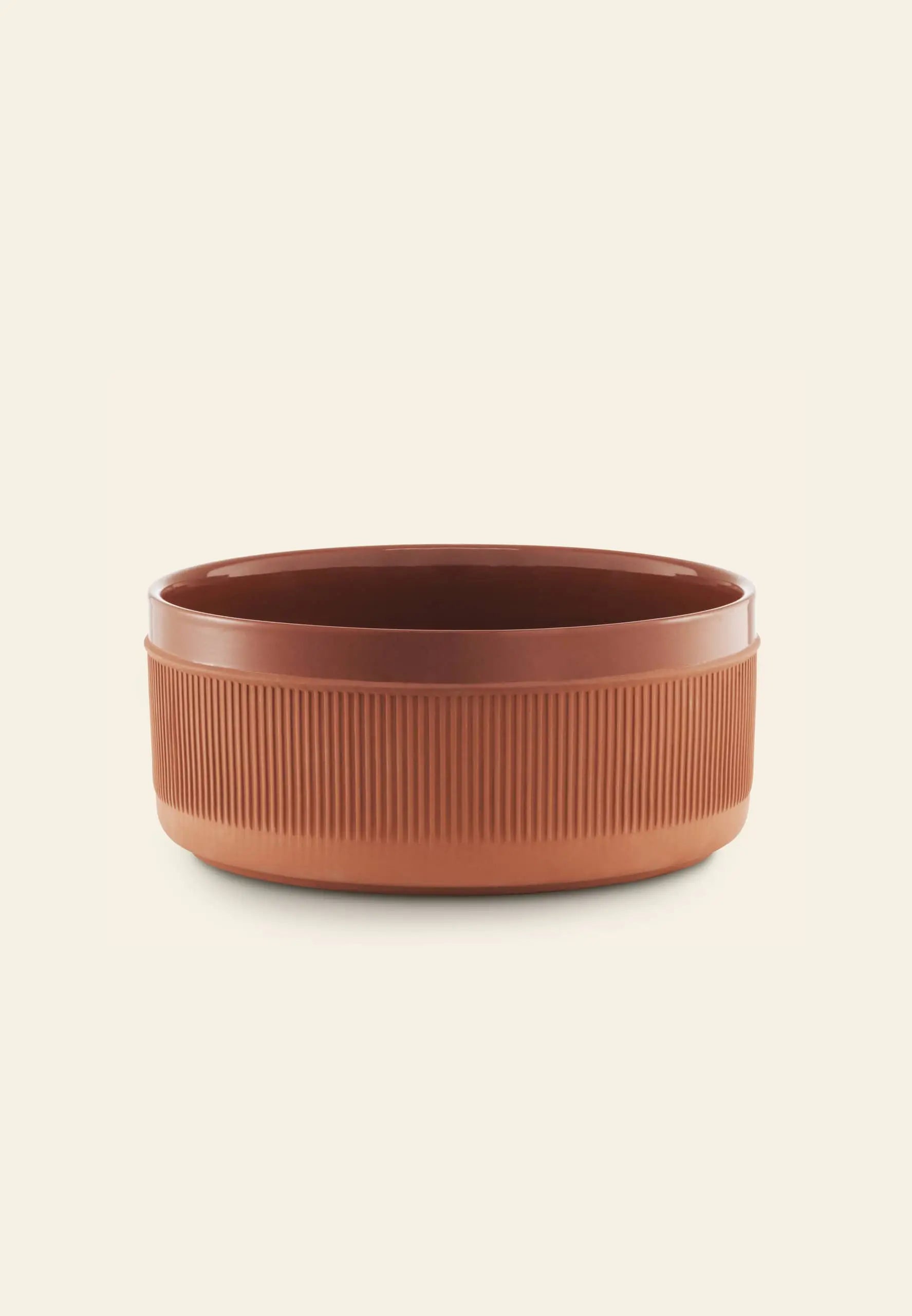 A round, brown Normann Copenhagen Junto Bowl, 24cm, with ribbed sides and rustic terracotta inspiration is set against a plain, light beige background.