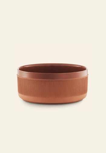 A round, brown Normann Copenhagen Junto Bowl, 24cm, with ribbed sides and rustic terracotta inspiration is set against a plain, light beige background.