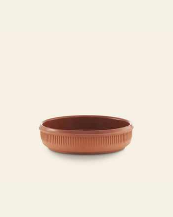 The Normann Copenhagen Junto Dish, 15.5cm, features a round, shallow terracotta design with ribbed sides inspired by the brand’s signature style. Set against a plain background, it’s both versatile and stylish for any setting.
