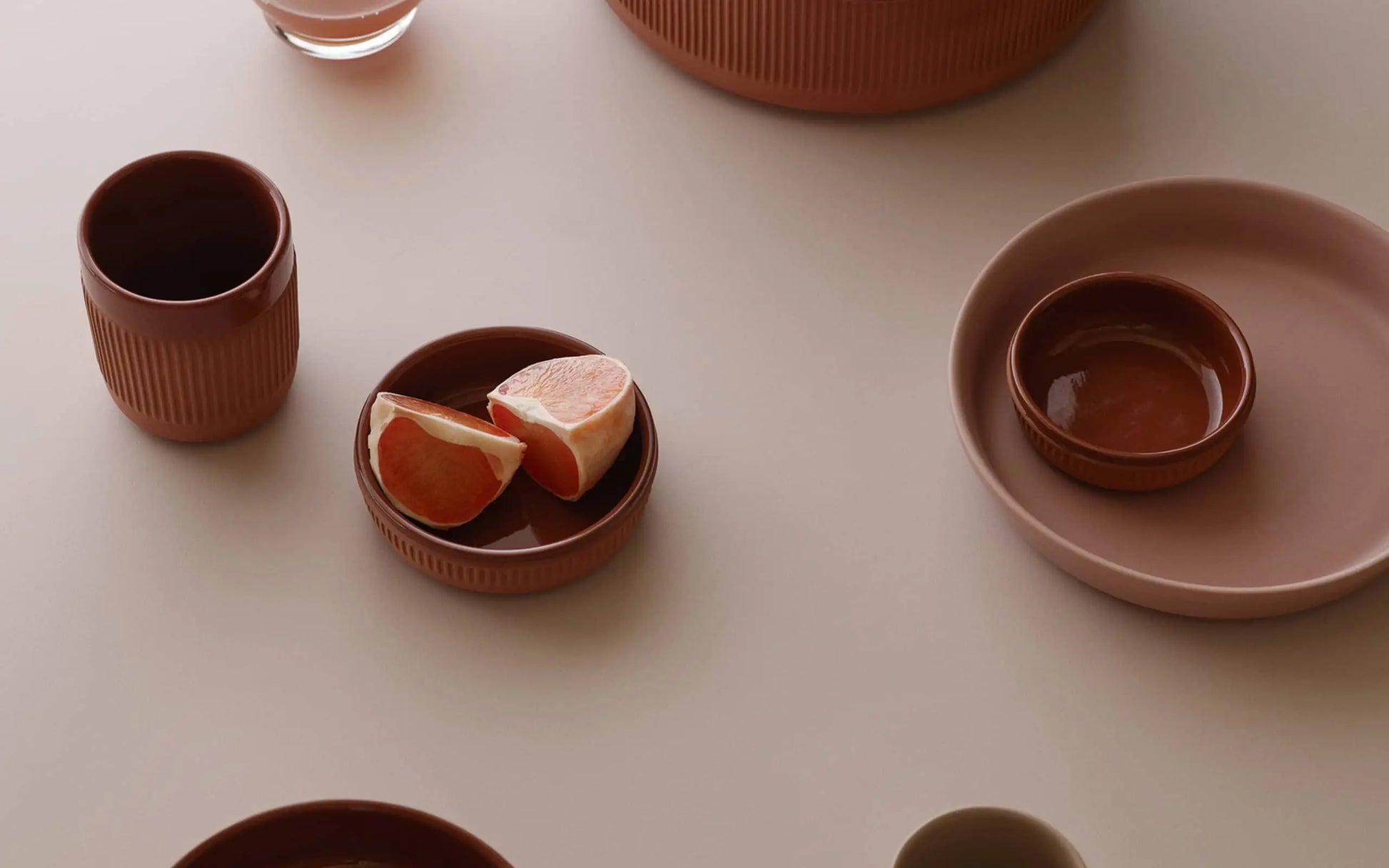 A minimalist table setting showcases Normann Copenhagen Junto Dish, 15.5cm, with earthy ceramic tones, grapefruit wedges, bowls, cups, and plates artfully arranged on a light surface.