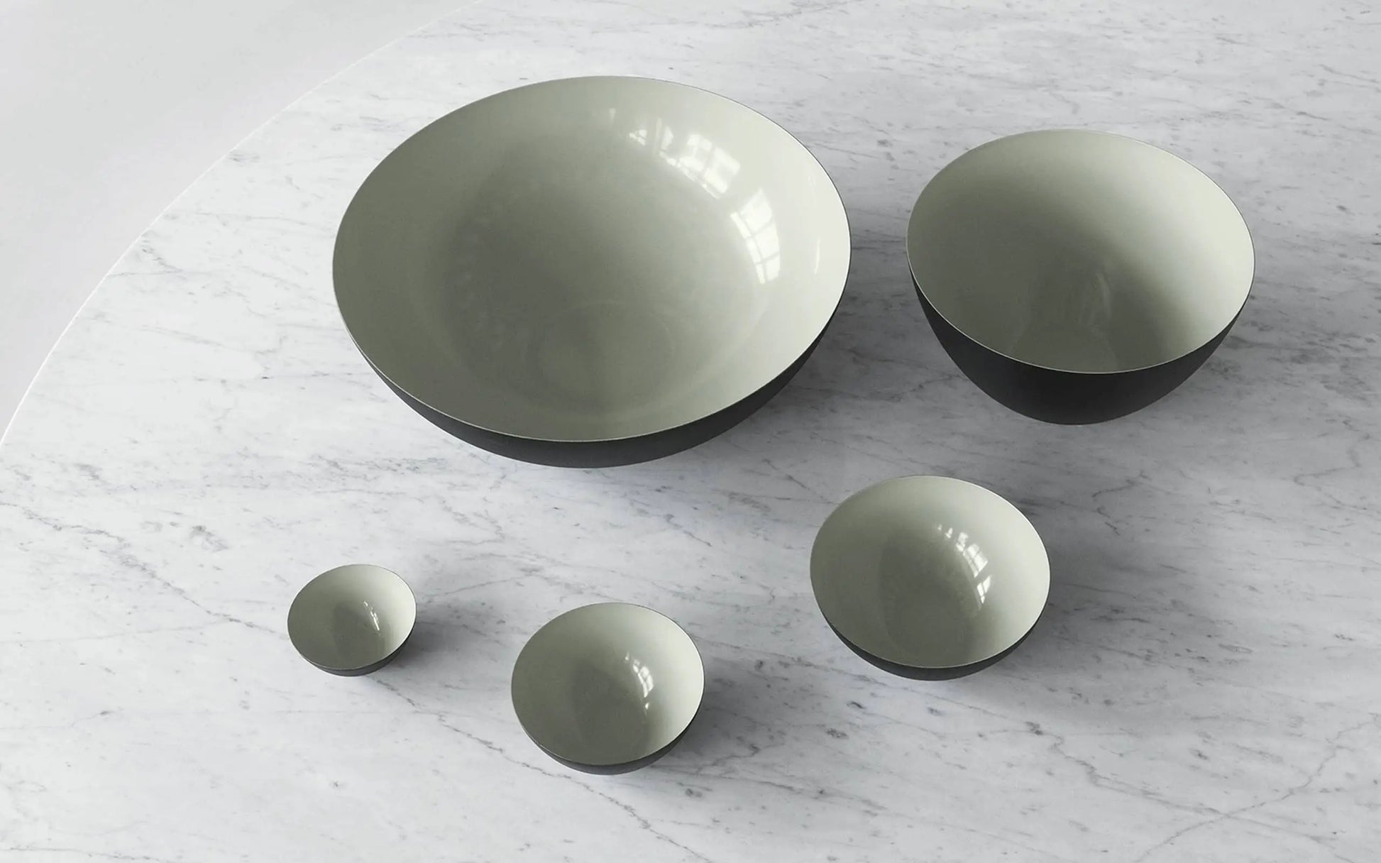 A Normann Copenhagen Krenit Bowl (12.5cm) with a glossy light gray interior and dark exterior rests on white marble—an elegant touch of Danish design.