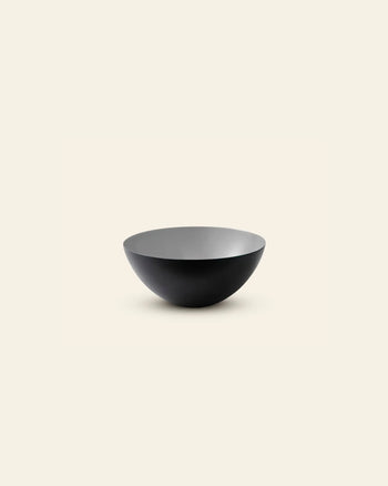 The Normann Copenhagen Krenit Bowl, 12.5cm, features a simple round form and matte black finish, exemplifying timeless Danish design. It is displayed against a plain light beige background.