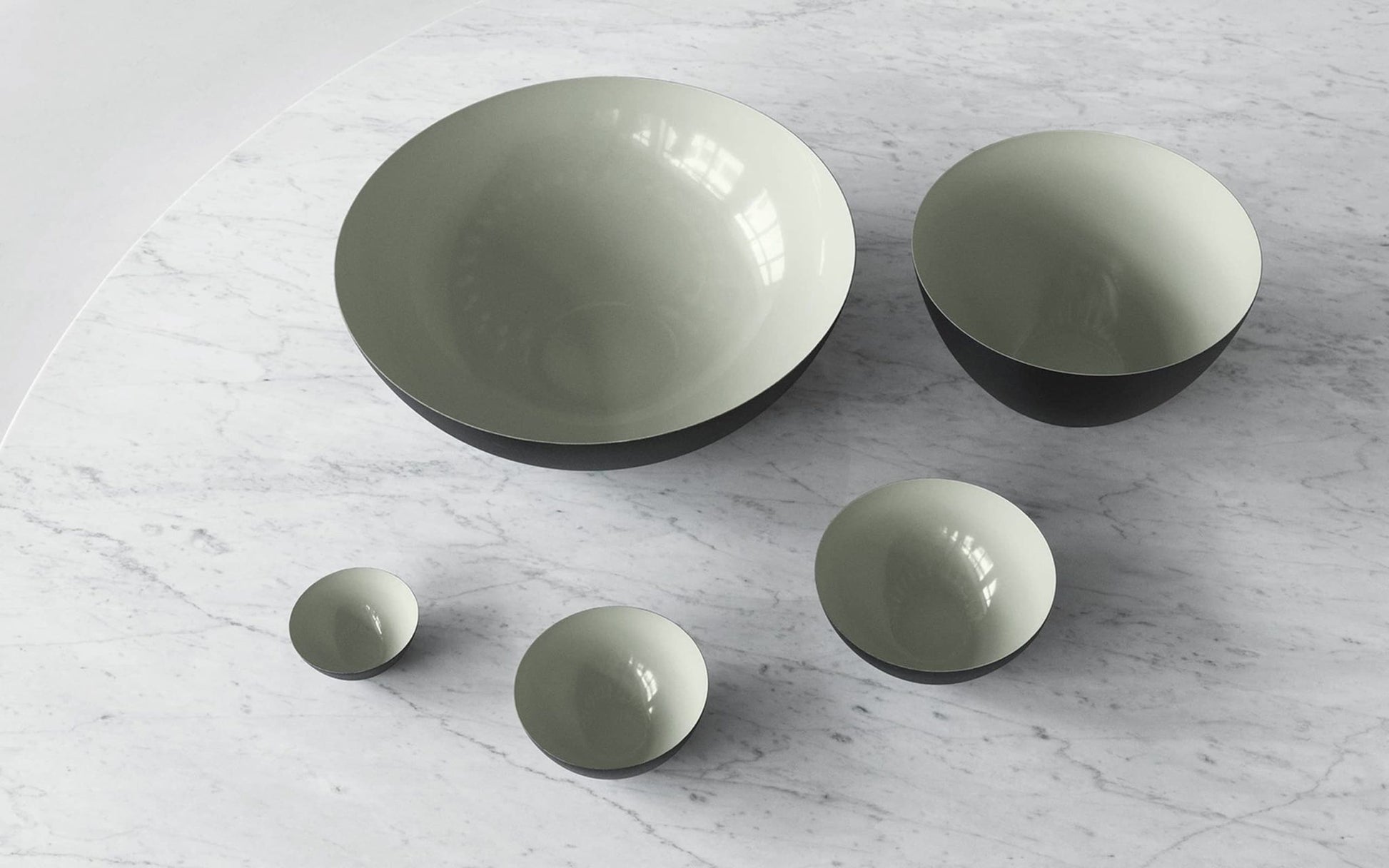 The Normann Copenhagen Krenit Bowl, 8.4cm, exemplifies Danish design with its iconic round shape, light grey interior, and dark exterior—displayed here among similar bowls on a white marble surface.