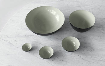 The Normann Copenhagen Krenit Bowl, 8.4cm, exemplifies Danish design with its iconic round shape, light grey interior, and dark exterior—displayed here among similar bowls on a white marble surface.
