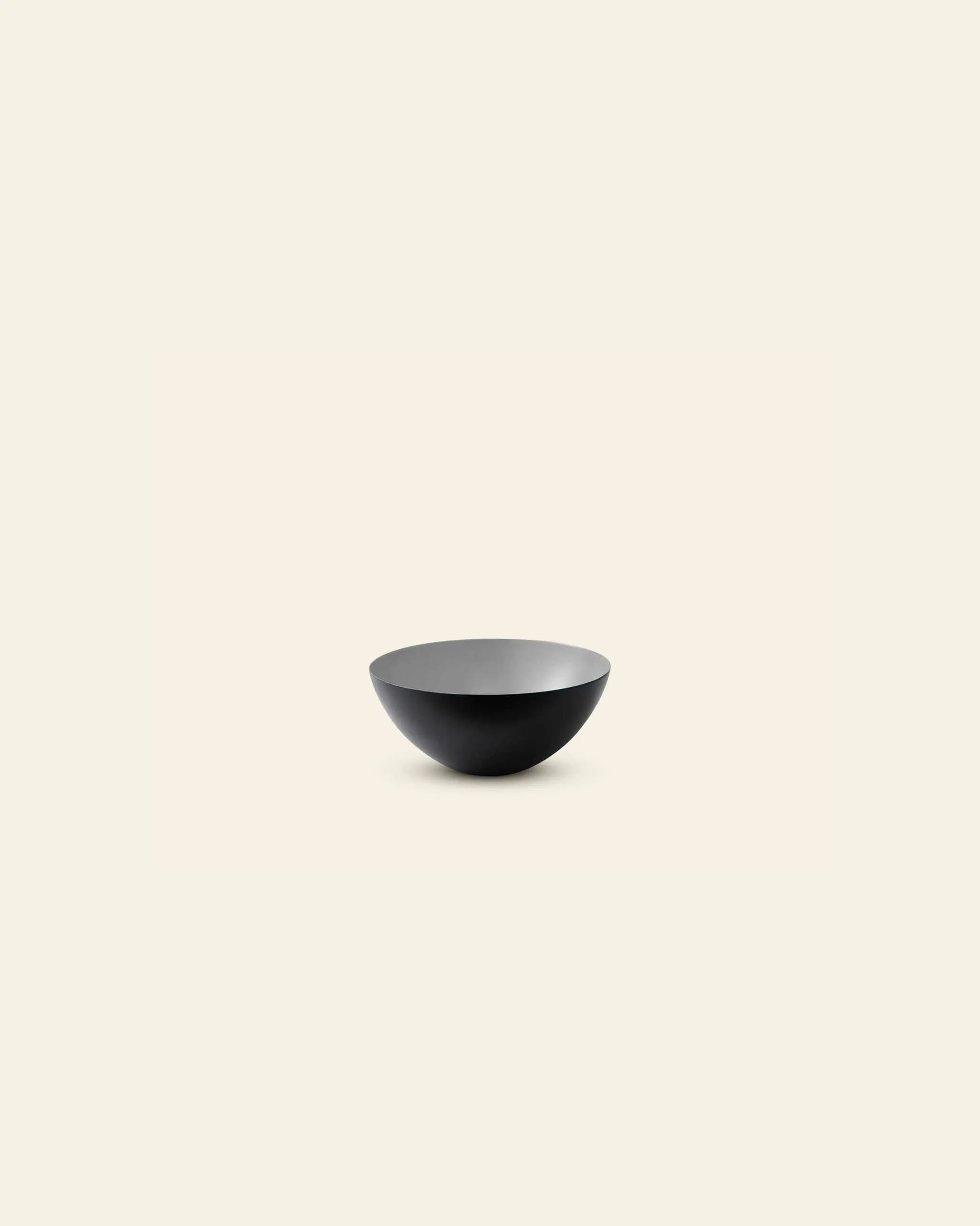 A minimalist photo of the Normann Copenhagen Krenit Bowl, 8.4cm—a black, shallow, round bowl—centered on a plain off-white background and showcasing timeless Danish design.