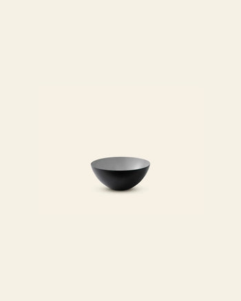 A minimalist photo of the Normann Copenhagen Krenit Bowl, 8.4cm—a black, shallow, round bowl—centered on a plain off-white background and showcasing timeless Danish design.