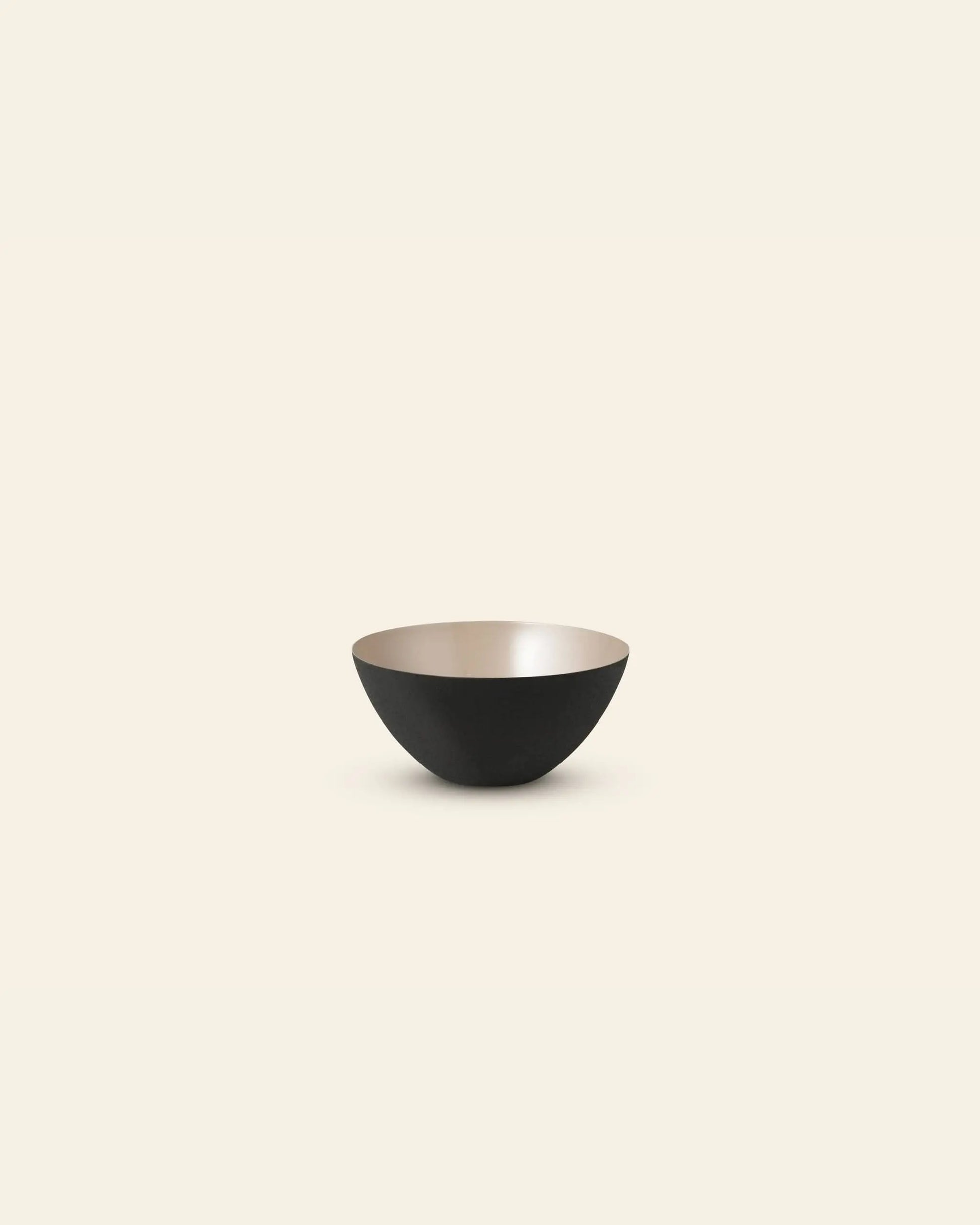 A minimalist image of the Normann Copenhagen Krenit Bowl, 8.4cm, featuring a black exterior and light beige interior, centered on a light cream background—an elegant tribute to classic Danish design by Normann Copenhagen.