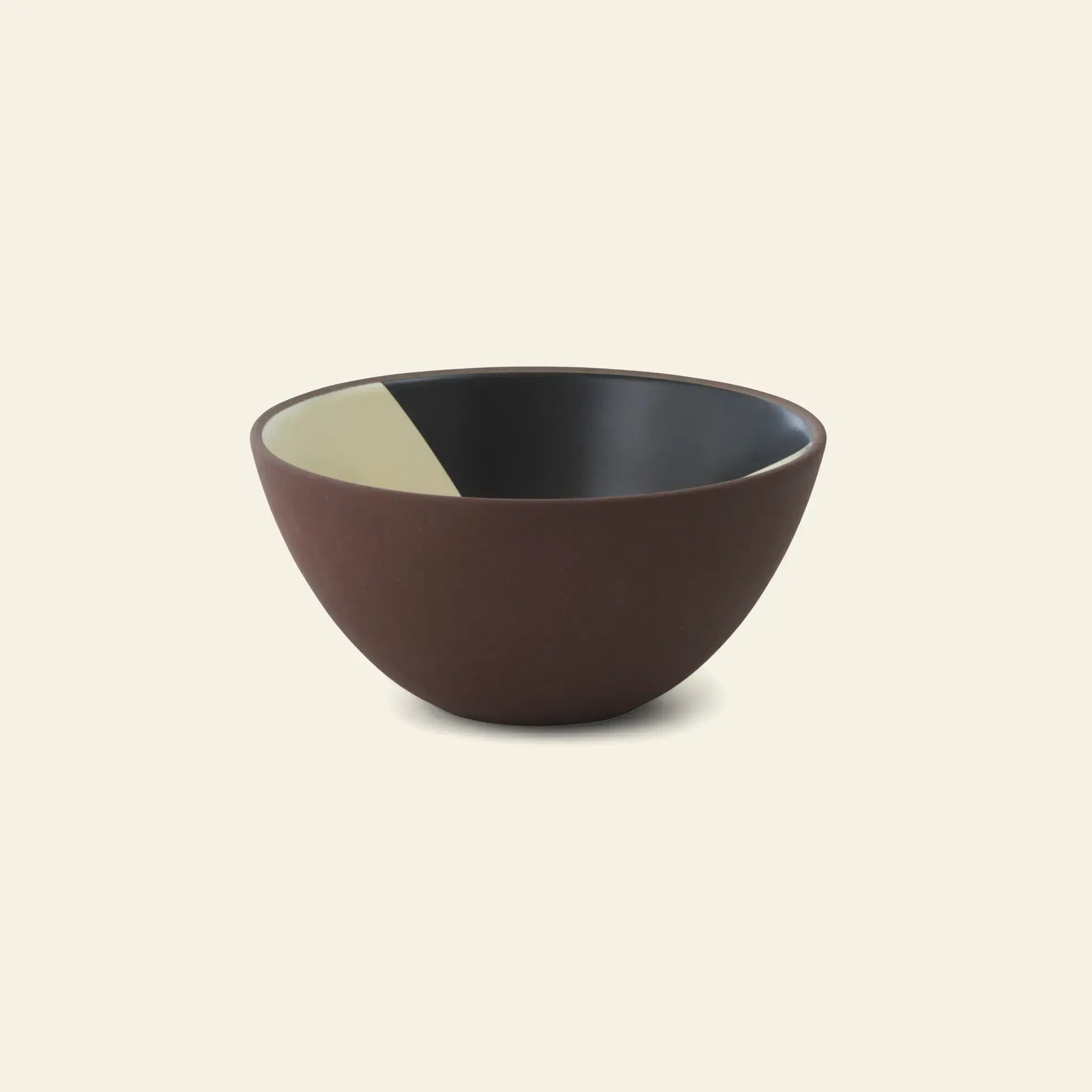 The Normann Copenhagen Line Bowl, 15cm, is a round, matte brown ceramic bowl made of red clay with a smooth finish and black interior accented by a light beige segment, set against a plain light beige background.